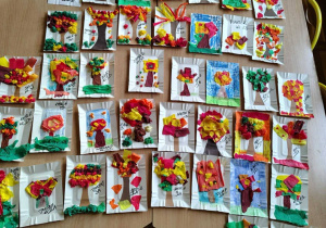 Kolorowe prace uczniów ze świetlicy przedstawiające jesienne drzewa wykonane z bibuły i papieru, ułożone na stole.