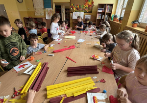 Dzieci w świetlicy szkolnej wykonują jesienne prace plastyczne z bibuły, siedząc przy długim stole i pracując nad kolorowymi drzewami.