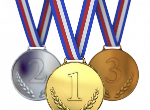 Trzy medale – złoty, srebrny i brązowy – zawieszone na biało-czerwono-niebieskich wstążkach, ustawione obok siebie.
