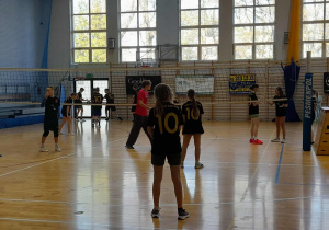 Uczniowie SP 13 w Pabianicach stoją na boisku do siatkówki w hali sportowej, ubrani w czarne koszulki wolontariatu, przygotowując się do meczu.