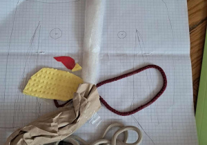 Płaski model układu pokarmowego wykonany z gąbek, papieru i sznurka na tle narysowanej sylwetki człowieka.