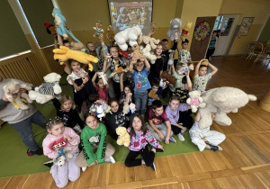 „Dzieci ze świetlicy pozują z pluszowymi misiami uniesionymi nad głowami podczas wspólnego świętowania Dnia Pluszowego Misia.”