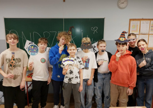 Grupa uczniów 6a i 6b pozuje z andrzejkowymi rekwizytami przed tablicą z napisem „ANDRZEJKI”.