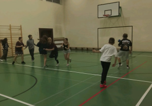 Uczniowie klas szóstych biegają po sali gimnastycznej, uczestnicząc w andrzejkowej grze w zbijaka.