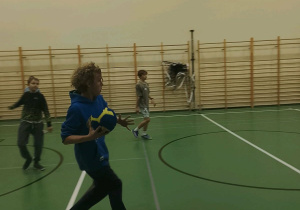 Chłopiec z klas szóstych biegnie z piłką po sali gimnastycznej w trakcie andrzejkowej zabawy w zbijaka.