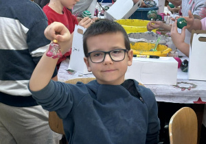 Uczeń klasy drugiej prezentuje do kamerki własnoręcznie ozdobioną bombkę w fabryce w Piotrkowie Trybunalskim.