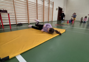 Uczennica turla się po żółtej macie jako element toru przeszkód w Świetlicowej Olimpiadzie Sportowej.
