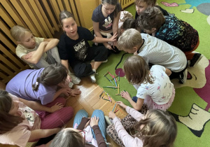 Dzieci siedzą w kręgu na dywanie i układają z kolorowych kredek różne kształty, ćwicząc współpracę podczas świetlicowego Dnia Kredki.