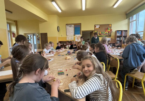 Uczniowie w świetlicy szkolnej podczas Światowego Dnia Postaci z Bajek lepią z plasteliny ulubionych bohaterów, siedząc przy dużym, wspólnym stole.