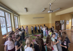 Grupa dzieci ustawiona w kręgu na dywanie w świetlicy szkolnej podczas listopadowej zabawy integracyjno-ruchowej.