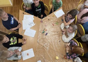 Grupa dzieci siedzących wokół stołu w świetlicy szkolnej, lepiących z plasteliny postacie z bajek w ramach listopadowych zajęć plastycznych.