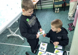 Dwóch chłopców z klasy 1b dobiera pary kart obrazkowych podczas gry dydaktycznej na warsztatach kreatywnej matematyki w bibliotece.