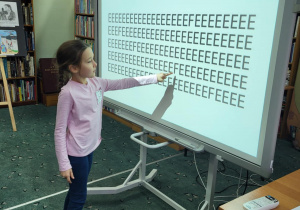 Dziewczynka z klasy 1b pokazuje na tablicy interaktywnej jedną z ukrytych literek F w ćwiczeniu rozwijającym spostrzegawczość.