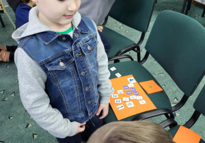 Dwóch chłopców z klasy 1b układa liczby na pomarańczowej planszy z kartonikami podczas warsztatów kreatywnej matematyki.