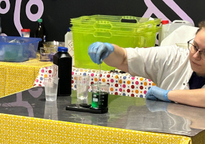 Prowadząca zajęcia ‘Naukowy misz-masz’ demonstruje doświadczenie chemiczne, mieszając zielony roztwór w zlewce przed uczniami klasy 7a.