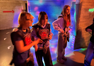 Trzy dziewczyny z 7a w kamizelkach laserowych stoją na arenie i rozmawiają po zakończonej rozgrywce.