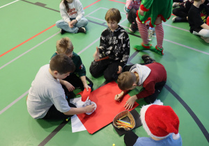 Uczniowie wykonują prace plastyczne podczas mikołajkowych zajęć na sali gimnastycznej.