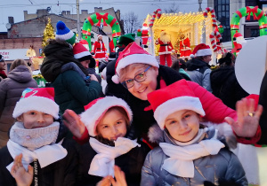 Nauczycielka i trzy uczennice SP 13 w czapkach Mikołaja pozują na tle świątecznej platformy podczas jarmarku.