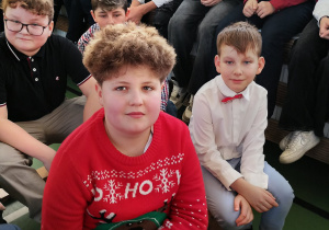 Uczniowie klasy czwartej siedzą na ławkach podczas szkolnej uroczystości.