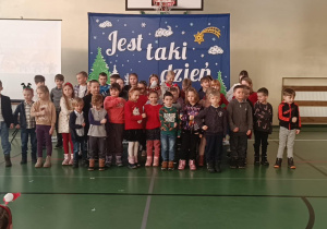 Zaproszeni goście z przedszkola stoją przed świąteczną dekoracją podczas szkolnej uroczystości.