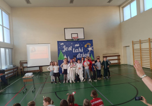 Uczniowie klasy 2 podczas występu świątecznego na sali gimnastycznej, przed dekoracją „Jest taki dzień”.