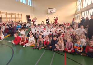 Uczniowie klas 1–3 i przedszkolaki siedzą na sali gimnastycznej podczas koncertu świątecznego.