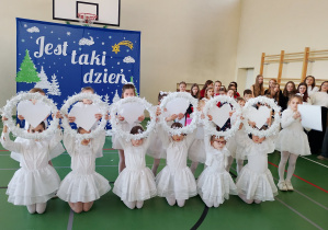 Uczennice w białych strojach prezentują taniec z sercami podczas koncertu świątecznego.