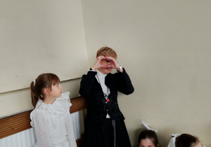 Dzieci w świątecznych strojach czekają za kulisami występu; jedno z nich w kostiumie bohatera jasełek żartobliwie udaje lornetkę z dłoni.