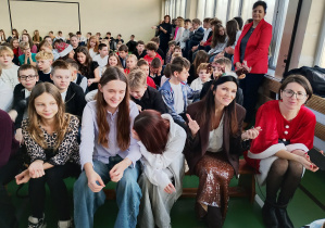 Uczniowie klas 4–8 oraz nauczyciele siedzą na ławkach w sali gimnastycznej podczas koncertu świątecznego.