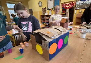 Dzieci w świetlicy szkolnej wykonują karmniki dla ptaków z kartonu podczas zajęć plastycznych.