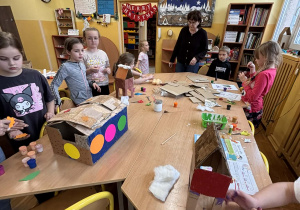 Dzieci w świetlicy szkolnej dekorują kartonowy karmnik dla ptaków przy wspólnym stole.