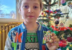 Uczeń świetlicy szkolnej prezentuje ozdobiony piernik na tle świątecznie udekorowanej choinki.