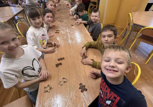 Dzieci w świetlicy szkolnej wspólnie przygotowują pierniki przy długim stole podczas zajęć kulinarnych.