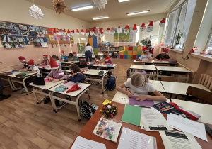 Uczniowie podczas zajęć plastycznych wykonują świąteczne prace w udekorowanej sali szkolnej.