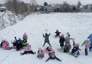 Uczniowie klasy 2b bawią się na śniegu na górce, korzystając z sanek i jabłuszek.