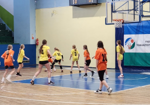 Mecz koszykówki dziewcząt – drużyna w żółtych koszulkach pod koszem rywali.