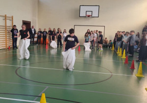 Uczniowie i nauczyciele uczestniczą w wyścigu w workach w sali gimnastycznej.