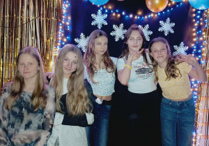 Pięć uczennic klasy szóstej pozuje przy świątecznej ściance ozdobionej balonami i śnieżynkami w czasie dyskoteki szkolnej.